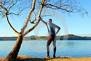 Silhouette of sport active man in running leggins and blue shirt at birch tree on beach. Calm water, island and sunny day