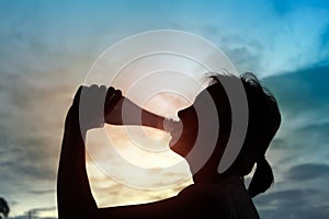 Silhouette of sport woman drinking water on sunset.