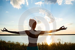 Silhouette of sportive girl practicing yoga in field at sunrise.