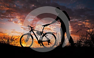 Silhouette of sports person cycling on the meadow on the beautiful sunset. Young man with camera and bicycle