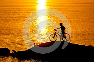 Silhouette of sportsman riding a bicycle on the beach. Colorful sunset cloudy sky in background