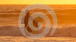 SILHOUETTE Sporty male tourist holding a surfboard while walking into deep water