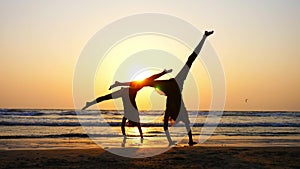 Silhouette of sporty young women practicing acrobatic element on the beach.