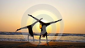 Silhouette of sporty young women practicing acrobatic element on the beach.