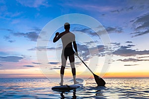 Silhouette of stand up paddle boarder paddling at sunset, sea