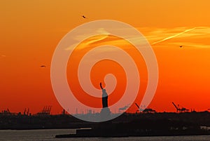 Silhouette of Statue of Liberty and Liberty Island in New York against an orange sunset sky