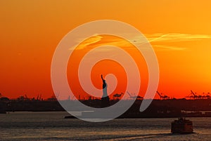 Silhouette of Statue of Liberty and Liberty Island in New York against an orange sunset sky.