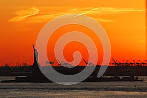 Silhouette of Statue of Liberty and Liberty Island in New York against an orange sunset sky