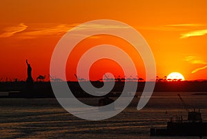 Silhouette of Statue of Liberty and Liberty Island in New York against an orange sunset sky