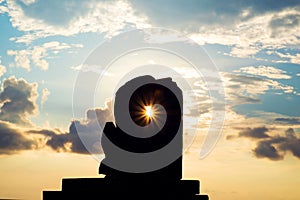 Silhouette statue with sun lens flare through the statue's hole in sunset