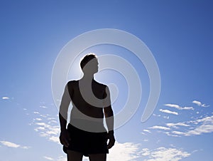 Silhouette of a strong man against blue summer sky.