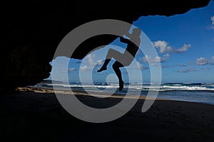 SILHOUETTE: Strong man climbs a big boulder near a stunning white sand beach.