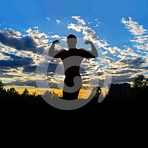 Silhouette of a strong muscular man on a background of sunset sky.