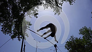 Silhouette of strong and muscular man doing gymnastic tricks on horizontal bar in slow motion on the blue sky background