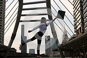 Silhouette of successful young Asian business woman raising her arms with document folder at urban building background.