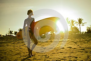 Silhouette with sun lens flare of young happy and attractive surfer girl carrying surf board posing on extreme backlight enjoying