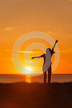 silhouette at sunset, person dancing and rejoicing against background of orange sky and sun