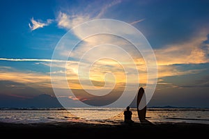 Silhouette of surf man sit with a surfboard on the beach.