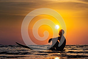 Silhouette of surf man sit on a surfboard. Surfing at sunset