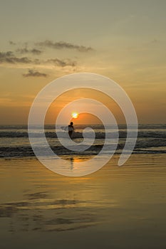 Silhouette of a Surfer carrying his surfboard on Kuta Beach at a golden Sunset