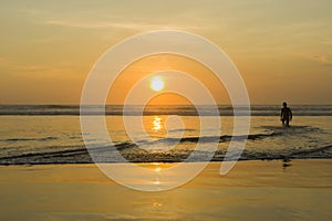 Silhouette of a Surfer carrying his surfboard on Kuta Beach at a golden Sunset