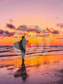 Silhouette of the surfer girl with surfboard on a beach at sunset. Surfer and ocean