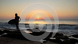 Silhouette of surfer girl with surfboard at the beach. Sunset time. Tegal Wangi beach, Bali, Indonesia