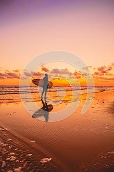 Silhouette with surfer girl and surfboard on a beach at warm sunset or sunrise. Surfer and ocean