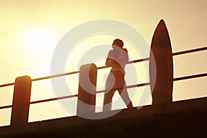 Silhouette of surfer on pier at sunrise with surfboard