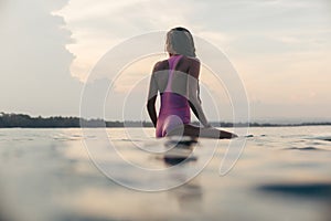 silhouette of surfer in pink swimsuit sitting on surfboard