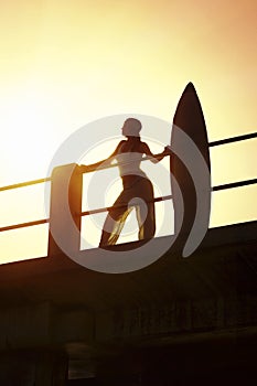 Silhouette of surfer standing on pier with surf board