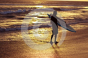 Silhouette of surfer with surfboard walking on the beach in sunset