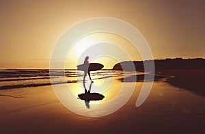 Silhouette of surfer walking along beach at sunrise