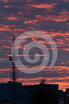 A silhouette of a tall telecommunication broadcasting tower against the vivid red sky on a cloudy summer evening