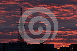 A silhouette of a tall telecommunication broadcasting tower against the vivid red sky on a cloudy summer evening