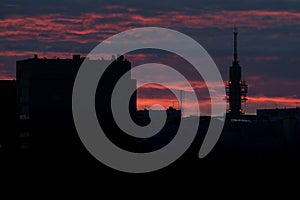 A silhouette of a tall telecommunication broadcasting tower against the vivid red sky on a cloudy summer evening