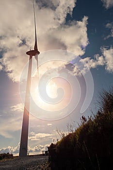 Silhouette of a tall wind generator against blue cloudy sky. Renewable source of energy in a plain field. Sun flare