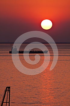 Silhouette of tank ship moored at anchor against red sunset sky