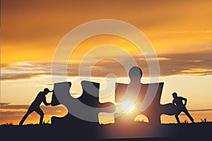 Silhouette of a team folding a puzzle against a sunset background, business and teamwork concept