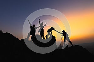 Silhouette Teamwork of four hiker helping each other on top of mountain climbing team beautiful sunrise. Teamwork friendship