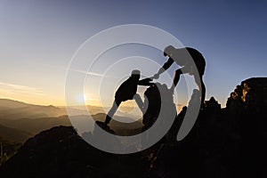 Silhouette Teamwork, Male hikers climbing up mountain cliff and one of them giving helping hand. People helping and, team work