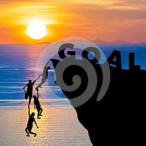 Silhouette teamwork of people climbs into cliff to reach the word GOAL sunrise (goal setting business concept)