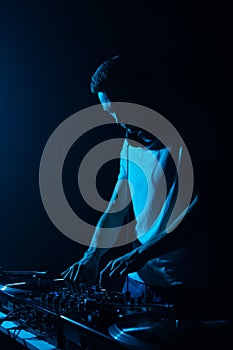 Silhouette of techno DJ playing music in night club. Cool young white man mixing musical tracks on stage