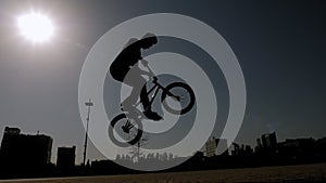 Silhouette of a teenage boy doing stunts on a BMX bike in a city Park.
