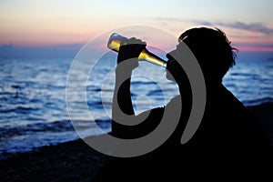 Silhouette teenager boy drinking beer on seacoast