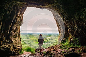 Silhouette of a teenager girl standing by a cave entrance, beautiful nature in the background. Travel, holiday and adventure