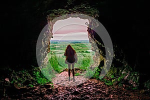 Silhouette of a teenager girl standing by a cave entrance, beautiful nature in the background. Travel, holiday and adventure