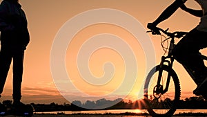 Silhouette of teenagers at sunrise. One boy rides on a self-balancing two-wheeled gyroscope and another young man on a bicycle.