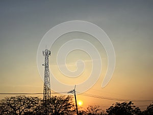 Silhouette of telecommunication tower, electrical power lines and tree branches during sunset