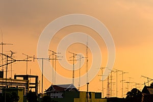 Silhouette, telecommunication towers with TV antennas and satellite dish in sunset. Many home TV antennas and satellite mounted